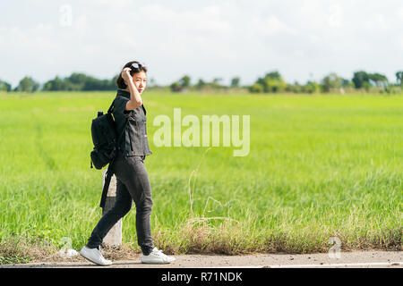 Woman with backpack hitchhiking along a road Stock Photo