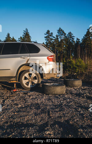 Changing of tire on a gravel field with a jack, with studded winter tires laying on the ground Stock Photo