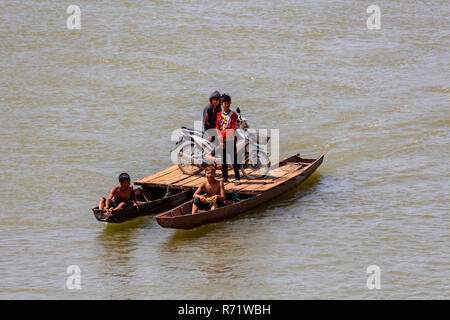 Don Daeng, Laos - April 27, 2018: Group of children transporting a scooter on a catamaran ferry made of two wooden canoes Stock Photo