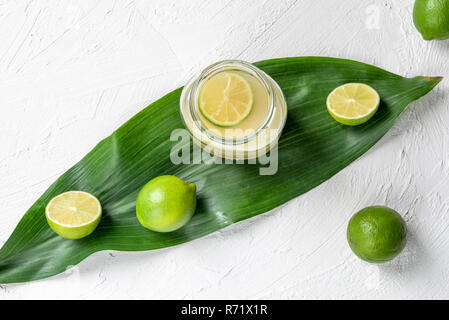 Fresh lemonade in a jar and green limes on a leaf. Above view with a white kitchen table and Stock Photo
