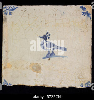 Animal tile with bird, three plumes on the head, blue decor on white ground, corner fill: ox head, marked, wall tile tile image ceramics pottery glaze tin glaze, in shape made baked glazed painted baked Wall tile with blue decor on white background. Animal tile with bird with three feathers on the head as possible. Possibly peacock with brushed tail Yellow-orange shard. Scraped earthenware Slightly slanted sides. Marked at the back In blue paint on the back: T wide letter with short trunk Rotterdam City center Stadsdriehoek Zandstraat indigenous pottery Originating from the Zandstraat Rotterda Stock Photo