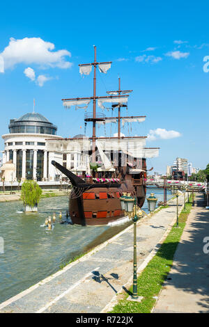 Galleon ship restaurant and bar on Vardar River, Government buildings behind, Skopje, Macedonia Stock Photo