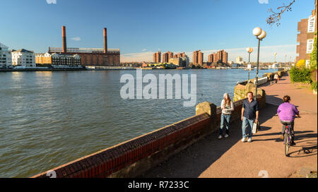 London, England, UK - March 16, 2014: Pedestrians and cyclists enjoy a sunny day on Battersea Riverside, with the River Thames and Chelsea's Lots Road Stock Photo