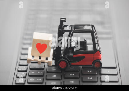 Forklift with red heart symbol on wooden block over laptop keyboard Stock Photo