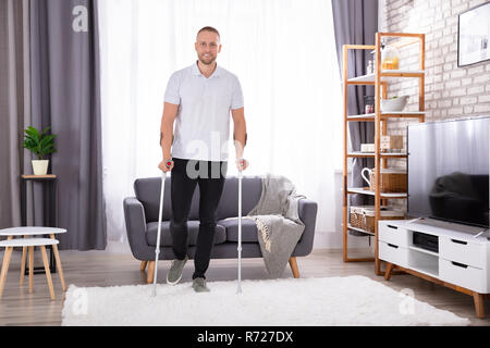 Disabled Young Man Using Crutches To Walk On Carpet Stock Photo