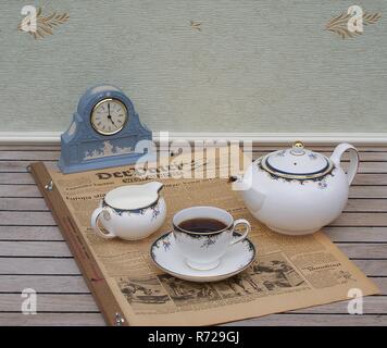 English tea set in front of a pale blue Wedgwood watch, Jasperware, with applied relief plate of white clay, on an old German daily newspaper Stock Photo