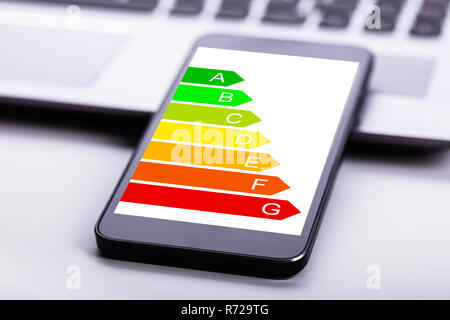 Close-up Of Laptop And Mobile Phone With Energy Efficiency Chart On Screen Over Desk Stock Photo