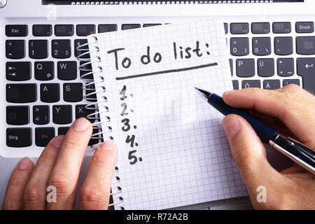 Close-up Of A Person's Hand Planning To Do List On Spiral Notepad Over Laptop Stock Photo