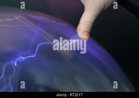 A plasma ball is used for studying high voltage electrical phenomena.  This shows the effect of a conducting object touching the ball. Stock Photo