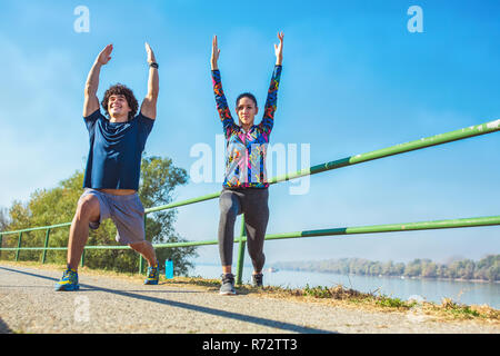 young fitness man and woman stretching in the park. Young couple warming up in morning. Stock Photo