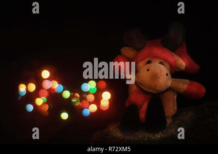 Little Christmas reindeer toy bear sitting on moss, in front of Christmas lights. Stock Photo