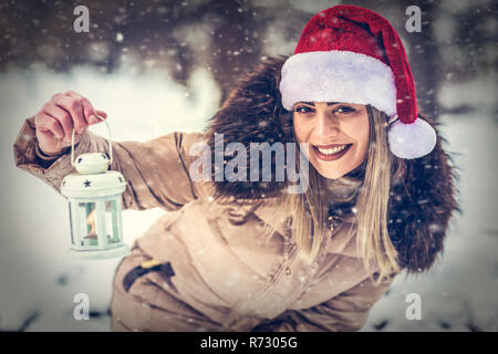 beautiful smiling girl in Santa hat on winter forest with Christmas lantern Stock Photo