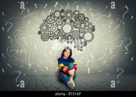 Pretty casual woman sitting on the floor and a huge gear brain above her head, positive thinking, question marks and mess as thoughts around. Concept  Stock Photo