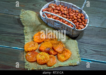 Dried apricots and peanuts in a wicker basket on a wooden table close-up Stock Photo