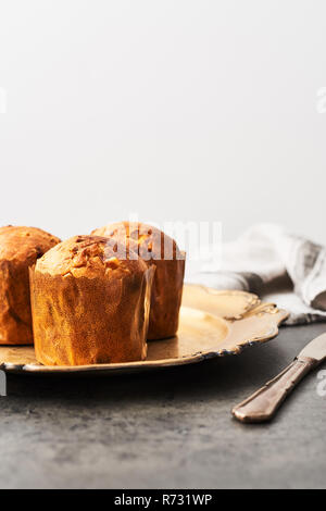 Traditional Christmas mini Panettone with raisins and dried fruits on a old golden serving plate over concrete table. Copy space for text. Stock Photo