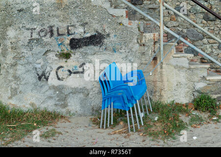 Stacked blue chairs, they are tied with chain and padlock to the railing of a staircase, on the wall it was written with paint, toilet and wc Stock Photo