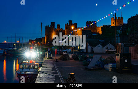 Conwy Castle and Quay on the River Conwy, North Wales. The bright lights come from the Nicola Faith Fishing Boat. Image taken in  Autumn 2018. Stock Photo