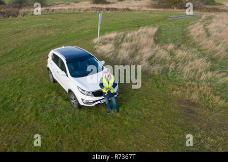 Drone SUAV pilot with remote controller in hand and wearing a hi viz jacket flying in a large field. Stock Photo
