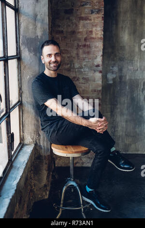 Man sitting on swivel stool by window Stock Photo
