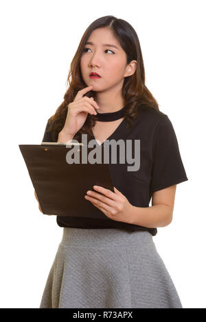 Young beautiful Asian businesswoman holding clipboard while thin Stock Photo