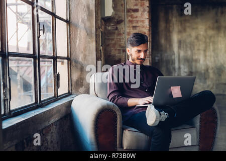 Man in armchair using laptop Stock Photo