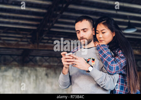 Woman looking over shoulder of man using smartphone Stock Photo