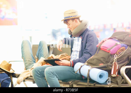 Young couple in departure lounge at airport, woman resting head on man's legs, man using digital tablet Stock Photo