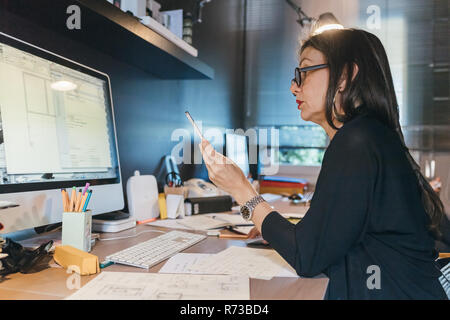 Woman using cellphone at desktop Stock Photo