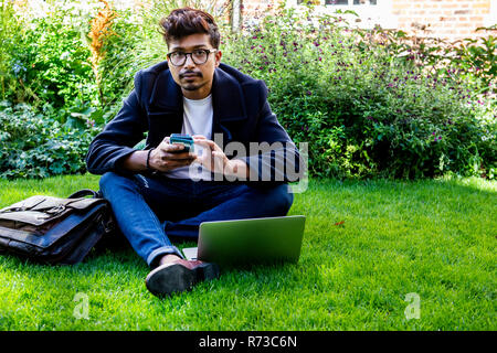 Businessman using smartphone and laptop on grass Stock Photo