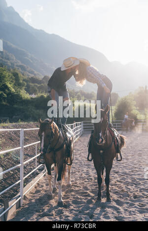 Cowgirl and boyfriend standing on horseback kissing in equestrian arena, Primaluna, Trentino-Alto Adige, Italy Stock Photo