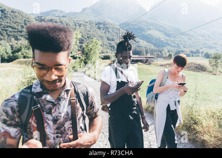 Young adult hikers on rural dirt track looking at smartphones,  Primaluna, Trentino-Alto Adige, Italy Stock Photo