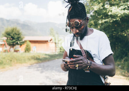 Cool young man on rural dirt track looking at smartphone, Primaluna, Trentino-Alto Adige, Italy Stock Photo