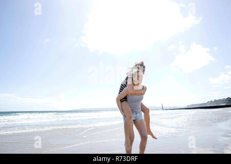 Sisters playing piggyback on beach Stock Photo