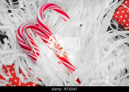 Christmas candy canes and red gift boxes illuminated by garland and placed on white paper sawdust Stock Photo