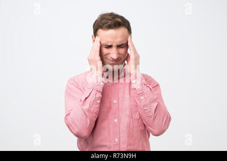 Handsome european man showing how much his head hurts, experiencing pain, looking exhausted Stock Photo