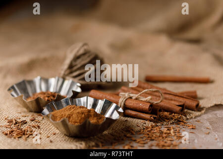 Crumbled cinnamon in baking tins and cinnamon sticks on textile under the burlap. Close-up. Stock Photo