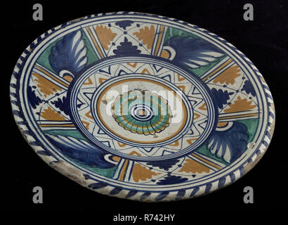 Majolica dish with polychrome rosette in the mirror, dish crockery holder soil find ceramic earthenware glaze tin glaze lead glaze, ring 10,2 hand turned fried glazed painted fried Dish with polychrome rosette in the mirror. Tapestry along the dish edge. Reverse glaze. Along the flag broad white band and band with an ornamental decor consisting of stacked beams in triangular shape and leaf ornaments Op baked archeology decorate home interior serving food Rotterdam Stock Photo