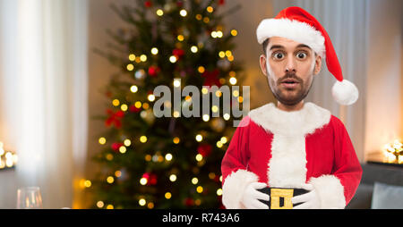 surprised man in santa clothes over christmas tree Stock Photo