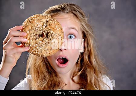 blond girl looking through a big bagel Stock Photo