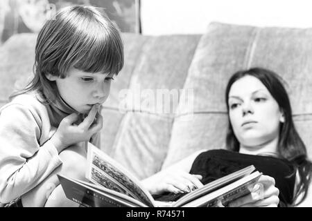 Young mother and her son lying on the couch and read stories from the book.