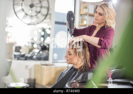 Hairdresser blow drying customer's hair in salon Stock Photo