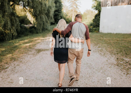 Romantic man and girlfriend strolling hand in hand on rural dirt track, rear view Stock Photo