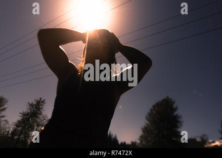 Young woman with hands on head against sunlit sky, backlit low angle view Stock Photo