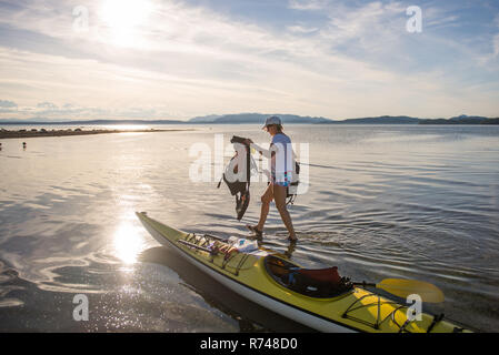 Mature female kayaker carrying life jackets from kayak, Quadra Island, Campbell River, Canada Stock Photo