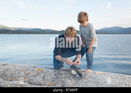 Boy and father preparing fish to grill on inlet rock, Aure, More og Romsdal, Norway Stock Photo