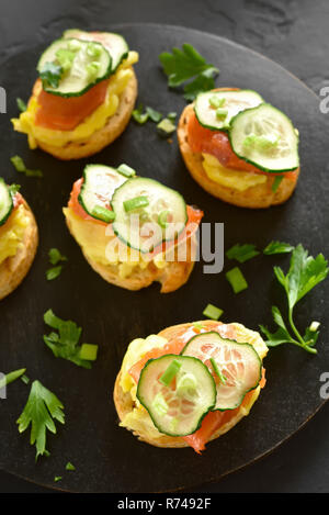 Toasted bread with salmon, scrambled eggs and cucumber slices on black wooden board. Top view Stock Photo