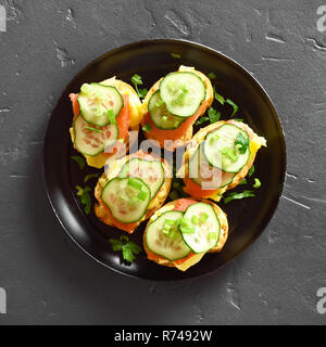 Sandwiches with salmon, scrambled eggs and cucumber slices on black stone background. Top view,flat lay Stock Photo