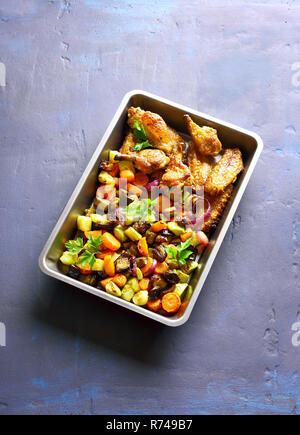 Grilled vegetables with chicken wings in baking tray on blue stone background with copy space. Stock Photo