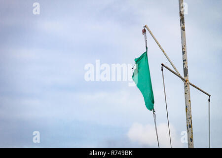 Tattered torn ripped green flag on a rusty iron pole against a cloudy sky background. Copy space. Stock Photo