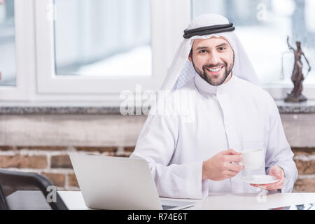 Arabian businessman drinking coffee near laptop in office Stock Photo